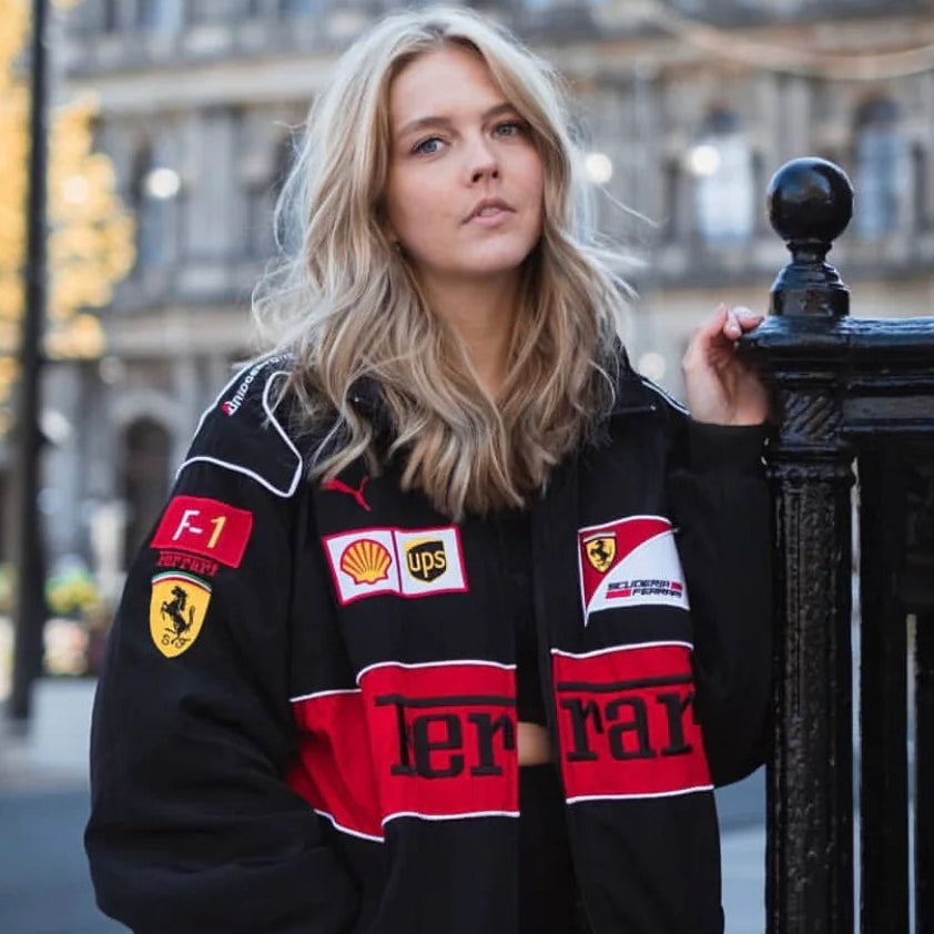 Person wearing a black racing jacket with various logos in an urban setting