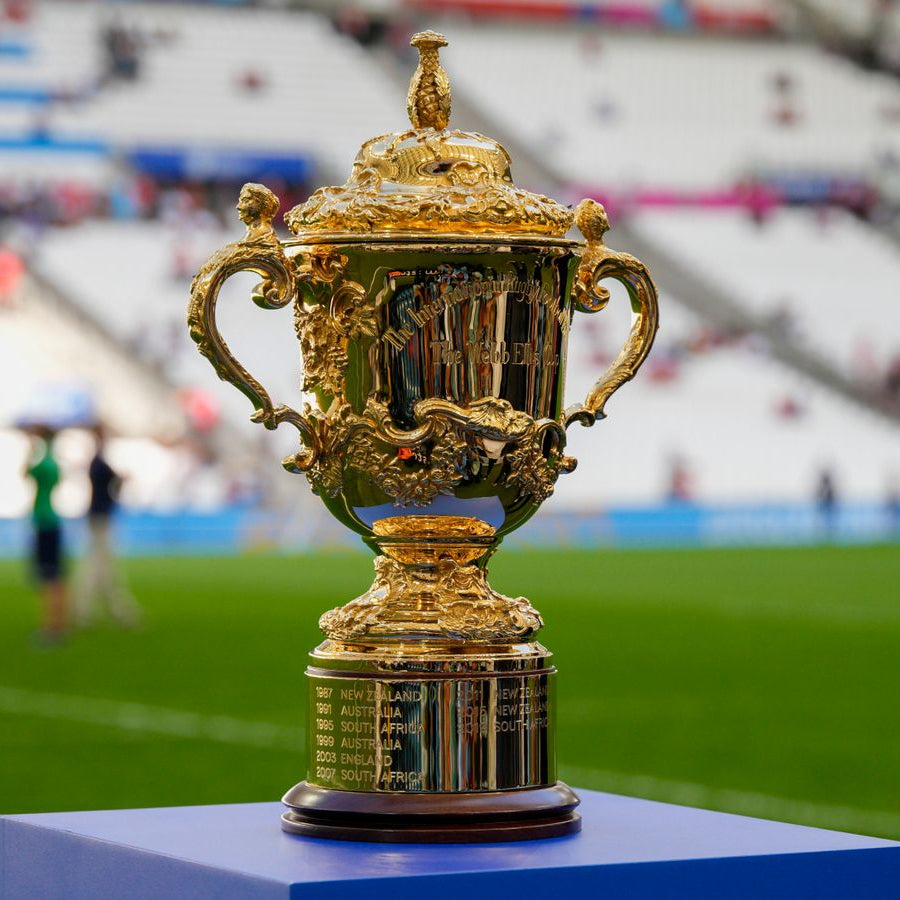 Gold rugby trophy on a pedestal with a blurred stadium background