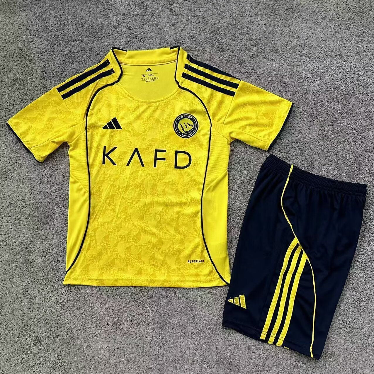 Adidas Al Nassr 2025/26 home kids football kit front view yellow jersey with navy shorts
