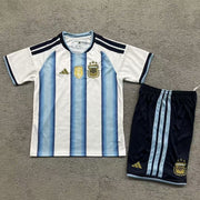 Adidas Argentina home kit 2026/27 kids set front view sky blue and white striped jersey with dark shorts
