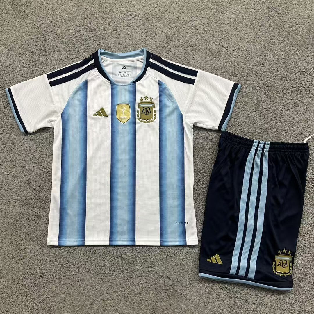 Adidas Argentina home kit 2026/27 kids set front view sky blue and white striped jersey with dark shorts
