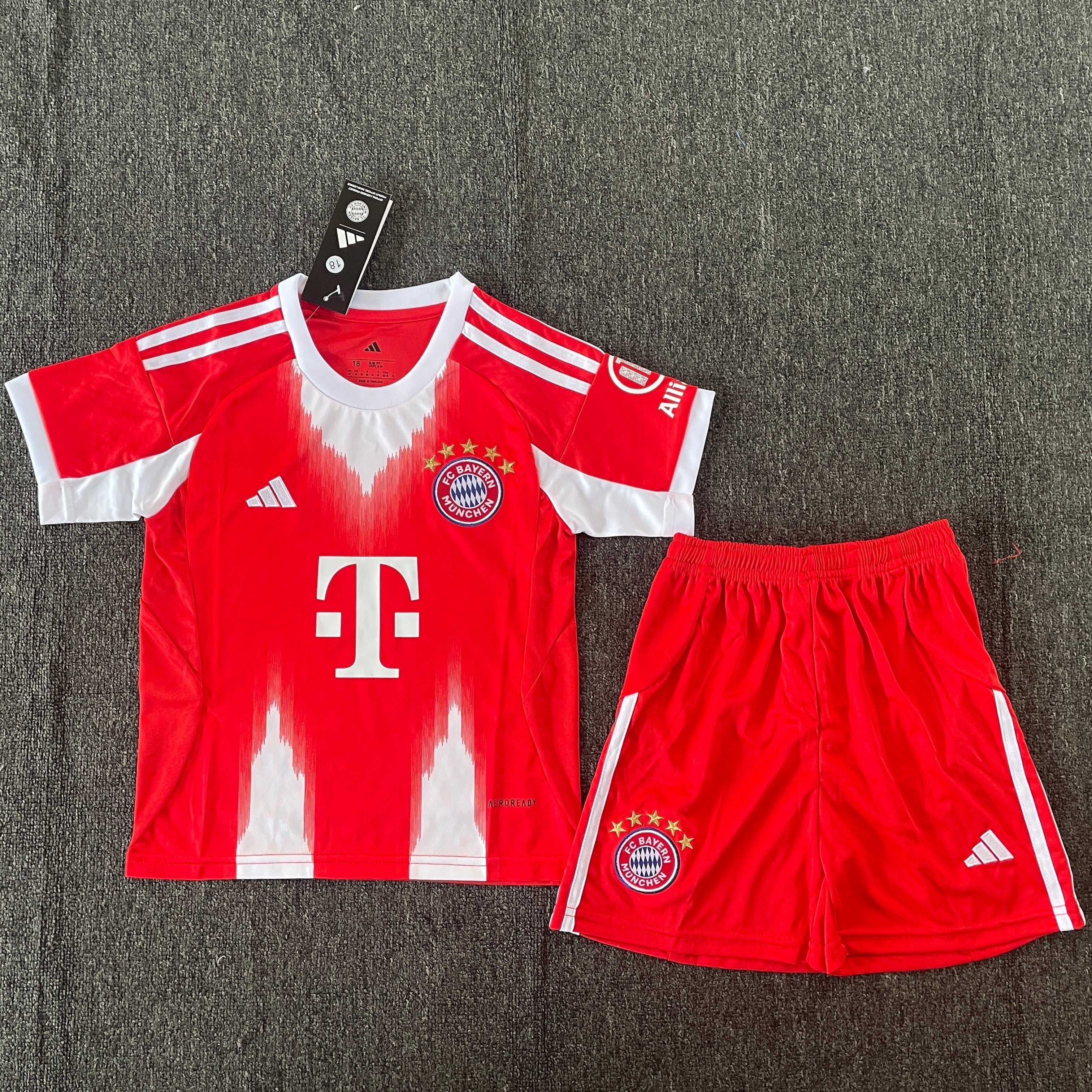 Adidas Bayern Munich home kit 2025 26 kids front view red jersey with white details and shorts
