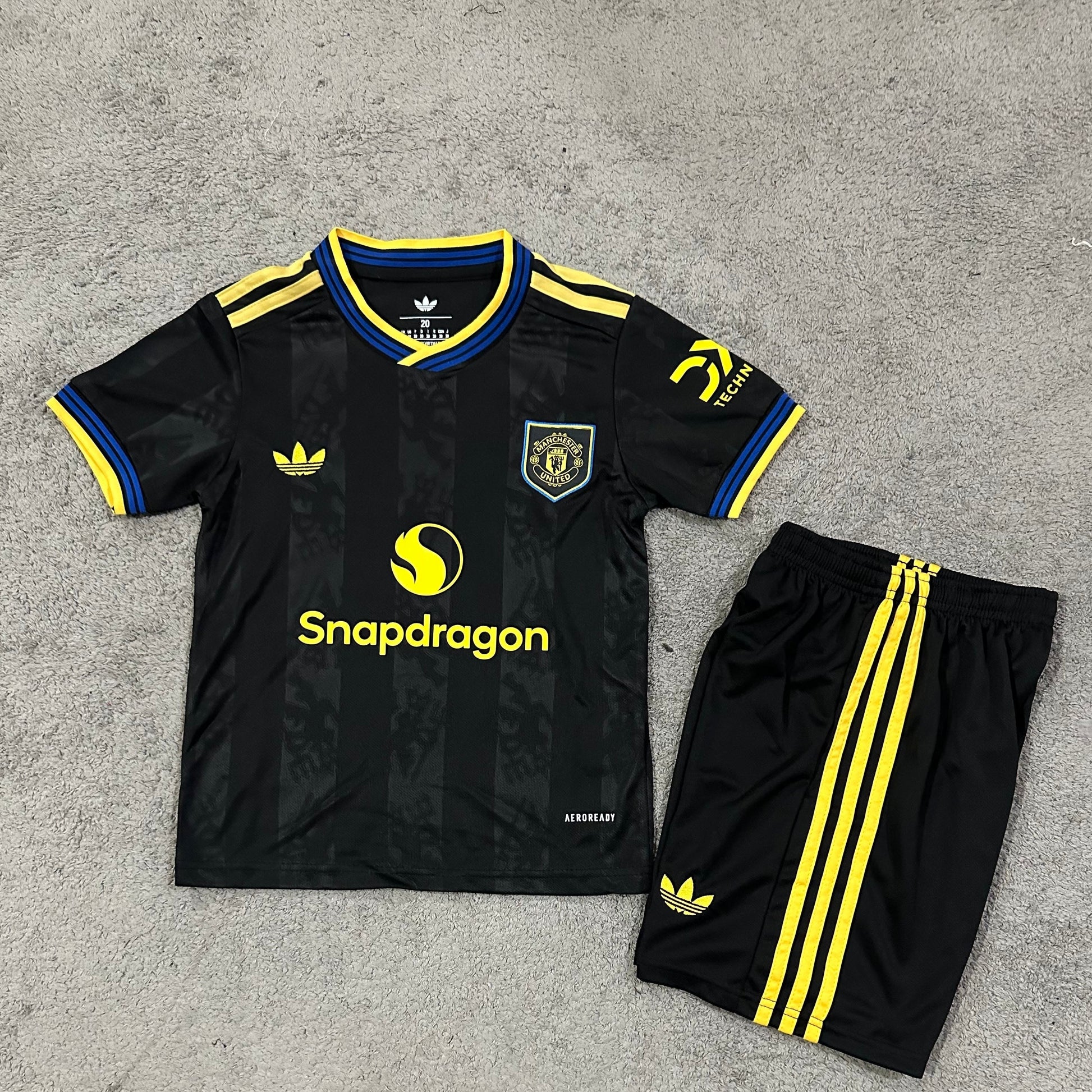 Adidas Manchester United away kit 2025 26 kids front view black jersey with yellow details and shorts
